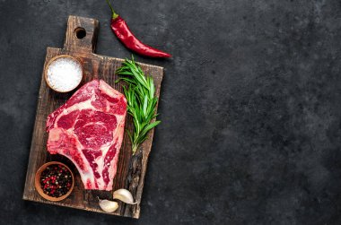 Baharatlı çiğ biftek ve ahşap kesim tahtasının üzerinde otlar. Koyu arkaplan