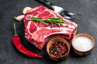 Baharatlı çiğ et ve siyah arka planda otlar.