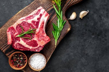 Baharatlı çiğ biftek ve ahşap kesim tahtasının üzerinde otlar. Koyu arkaplan