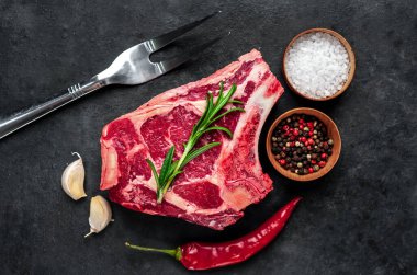 Baharatlı çiğ et ve siyah arka planda otlar.