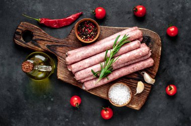 Baharatlı, sebzeli ve otlu çiğ sosisler bir şişe zeytinyağıyla ahşap kesme tahtasının üzerinde. Koyu arkaplan.