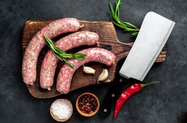 Ahşap kesme tahtasının üzerinde baharatlı ve otlu çiğ sosisler..