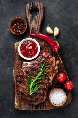 Ahşap kesme tahtasının üzerinde baharatlı, sebzeli ve otlu ızgara biftek..