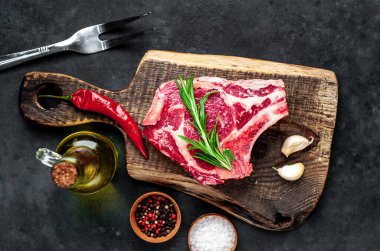 Baharatlı çiğ biftek ve ahşap kesim tahtasının üzerinde otlar. Koyu arkaplan