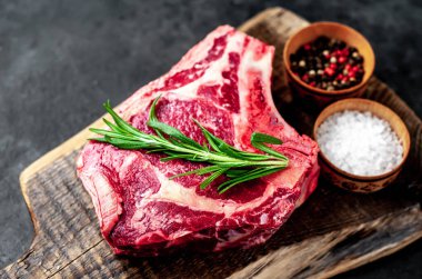 Baharatlı çiğ biftek ve ahşap kesim tahtasının üzerinde otlar. Koyu arkaplan