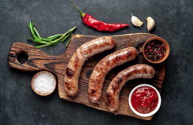 Baharatlı ve otlu ızgara sosisler kesme tahtasında koyu arka planda.