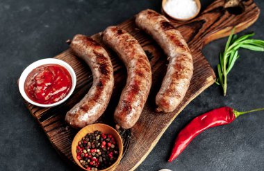 Baharatlı ve otlu ızgara sosisler kesme tahtasında koyu arka planda.