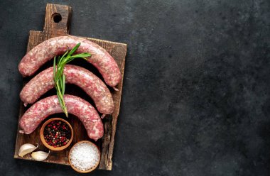 Ahşap kesme tahtasının üzerinde baharatlı ve otlu çiğ sosisler..