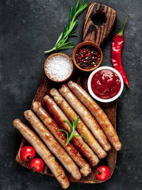 Kesme tahtasının üzerinde baharatlı, otlu ve sebzeli ızgara sosisler.