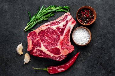 Baharatlı çiğ et ve siyah arka planda otlar.