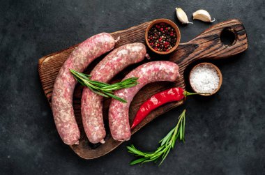 Ahşap kesme tahtasının üzerinde baharatlı ve otlu çiğ sosisler..