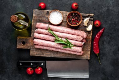 Baharatlı, sebzeli ve otlu çiğ sosisler tahta kesme tahtasının üzerinde satırdan bir bıçakla. Koyu arkaplan.