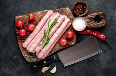 Baharatlı, sebzeli ve otlu çiğ sosisler tahta kesme tahtasının üzerinde satırdan bir bıçakla. Koyu arkaplan.