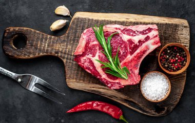 Baharatlı çiğ biftek ve ahşap kesim tahtasının üzerinde otlar. Koyu arkaplan