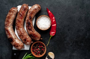 Baharatlı ve otlu ızgara sosisler ve siyah arka planda bir satır bıçağı..