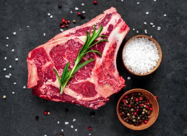 Baharatlı çiğ et ve siyah arka planda otlar.