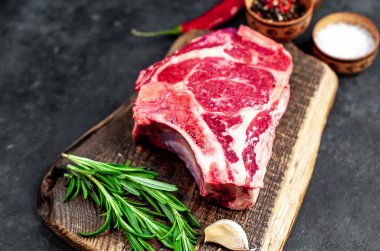 Baharatlı çiğ biftek ve ahşap kesim tahtasının üzerinde otlar. Koyu arkaplan