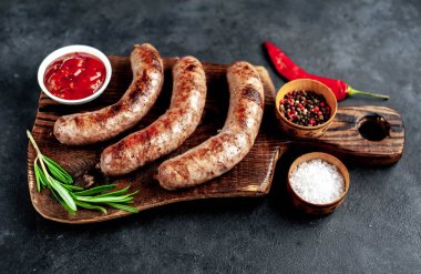 Baharatlı ve otlu ızgara sosisler kesme tahtasında koyu arka planda.