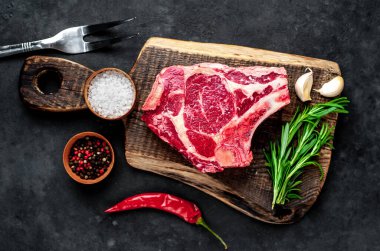 Baharatlı çiğ biftek ve ahşap kesim tahtasının üzerinde otlar. Koyu arkaplan