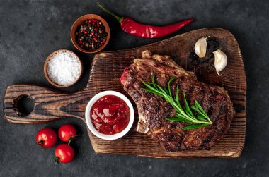 Ahşap kesme tahtasının üzerinde baharatlı, sebzeli ve otlu ızgara biftek..