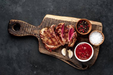 Ahşap kesme tahtasının üzerinde baharatlı, sebzeli ve otlu ızgara biftek..