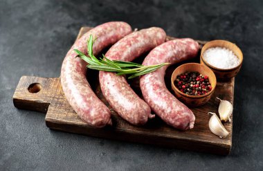 Ahşap kesme tahtasının üzerinde baharatlı ve otlu çiğ sosisler..