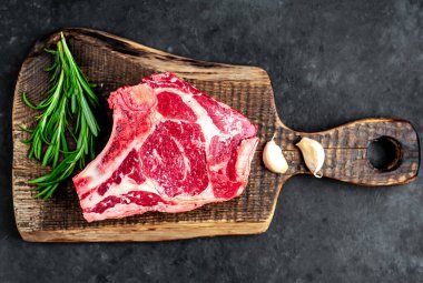 Baharatlı çiğ biftek ve ahşap kesim tahtasının üzerinde otlar. Koyu arkaplan