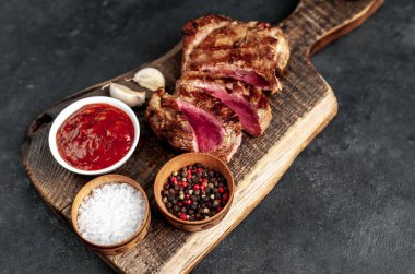 Ahşap kesme tahtasının üzerinde baharatlı, sebzeli ve otlu ızgara biftek..