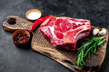 Baharatlı çiğ biftek ve ahşap kesim tahtasının üzerinde otlar. Koyu arkaplan