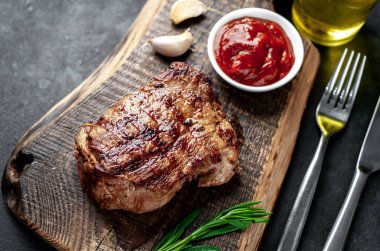 Ahşap kesme tahtasının üzerinde baharatlı, sebzeli ve otlu ızgara biftek..