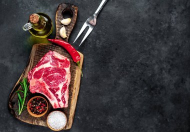 Baharatlı çiğ biftek ve ahşap kesim tahtasının üzerinde otlar. Koyu arkaplan