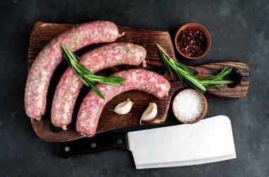 Ahşap kesme tahtasının üzerinde baharatlı ve otlu çiğ sosisler..