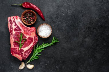 Baharatlı çiğ et ve siyah arka planda otlar.