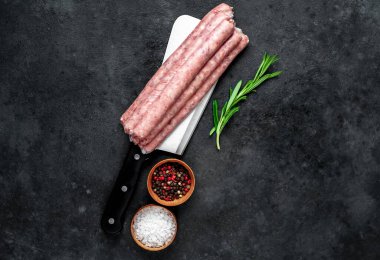 Baharatlı, sebzeli ve otlu çiğ sosisler siyah arka planda bir satır bıçağında..