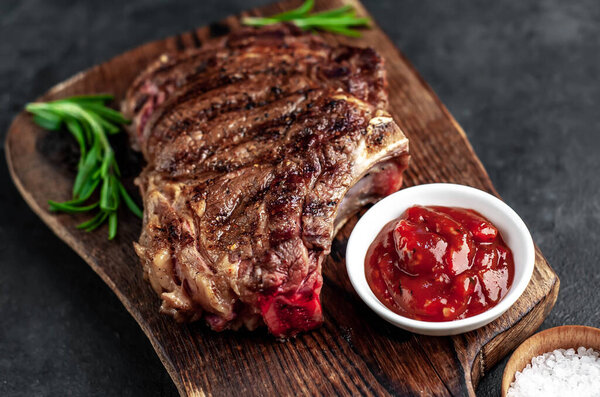 Grilled steak with spices and herbs on a wooden cutting board with dark background.