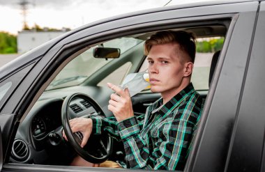 Genç yakışıklı beyaz adam arabasında otururken maskesini çıkarıyor.