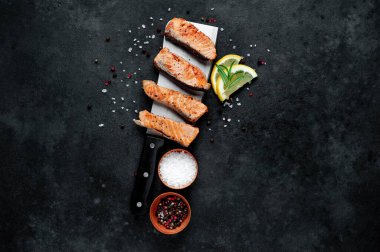 Limon dilimli ızgara somon parçaları ve koyu arkaplanda baharatlar. 