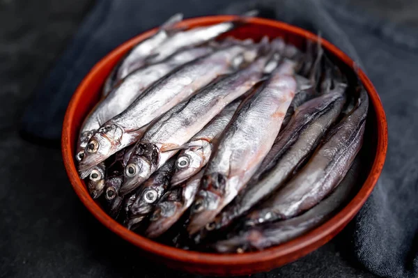 Top view on smelt fishes in a bowl with spices on dark background