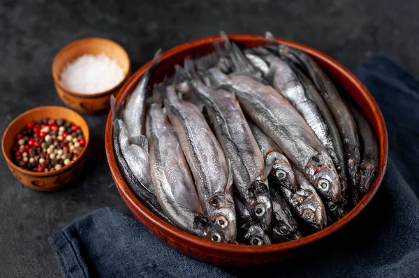 Top view on smelt fishes in a bowl with spices on dark background