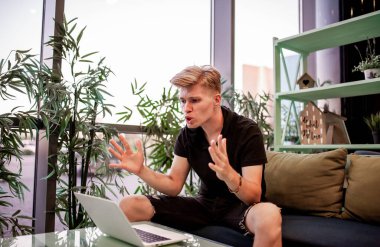 Kafeteryadaki masada otururken dizüstü bilgisayarla çalışan genç bir adam.