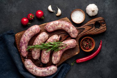 Izgara için çiğ sosis ve arka plandaki kesme tahtasındaki baharatlar.