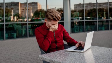 Genç bir adam sokakta bir masada oturuyor ve dizüstü bilgisayarda çalışıyor..