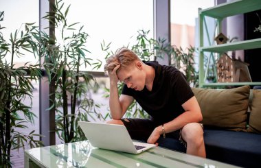 Kafeteryadaki masada otururken dizüstü bilgisayarla çalışan genç bir adam.