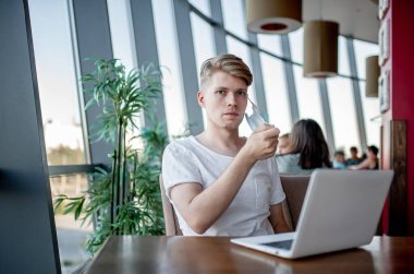 Maskeli yakışıklı genç adam, kafede dizüstü bilgisayarla çalışıyor. 