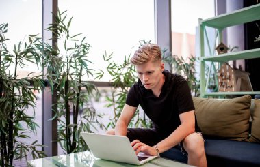 Kafeteryadaki masada otururken dizüstü bilgisayarla çalışan genç bir adam.