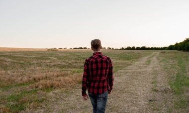 Tişörtlü bir çiftçi gün batımında bir tarlada duruyor.