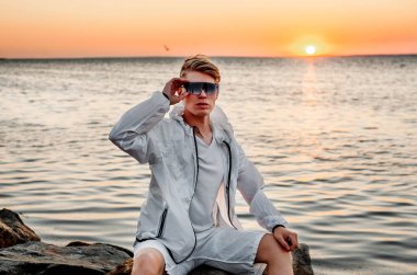 Beyaz elbiseli bir adam deniz kenarında gün batımına bakıyor.