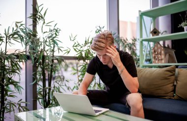 Kafeteryadaki masada otururken dizüstü bilgisayarla çalışan genç bir adam.