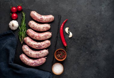 Izgara için çiğ sosis ve arka plandaki kesme tahtasındaki baharatlar.