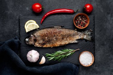 Taş zeminde baharat ve malzemelerle kızarmış balık alabalığı.